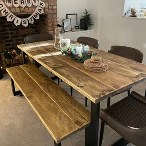 May include: A rustic wooden dining table with black metal legs and a matching bench. The table is set with a centrepiece of greenery and candles. The table is surrounded by chairs with brown leather upholstery.