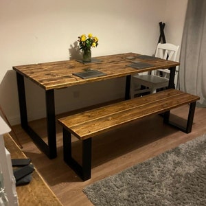 May include: A rustic wooden dining table with black metal legs and a matching bench. The table has a distressed wood finish and is perfect for a farmhouse or industrial style dining room.