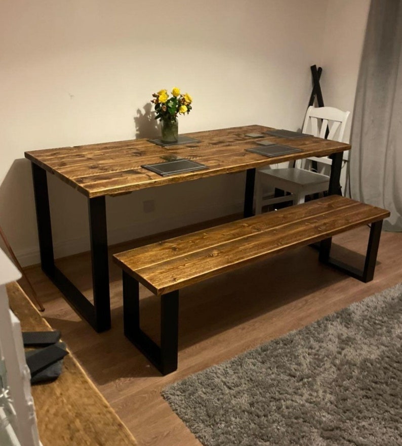 May include: A rustic wooden dining table with black metal legs and a matching bench. The table has a distressed wood finish and is perfect for a farmhouse or industrial style dining room.