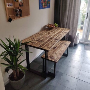 May include: A rustic wooden table and bench set with black metal legs. The table and bench have a distressed wood finish and are ideal for a dining area or kitchen.