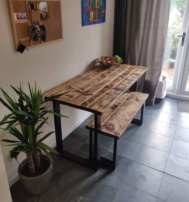May include: A rustic wooden table and bench set with black metal legs. The table and bench have a distressed wood finish and are ideal for a dining area or kitchen.