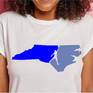 May include: A white t-shirt with a blue and light blue silhouette of the state of North Carolina with a basketball player shooting a basketball.