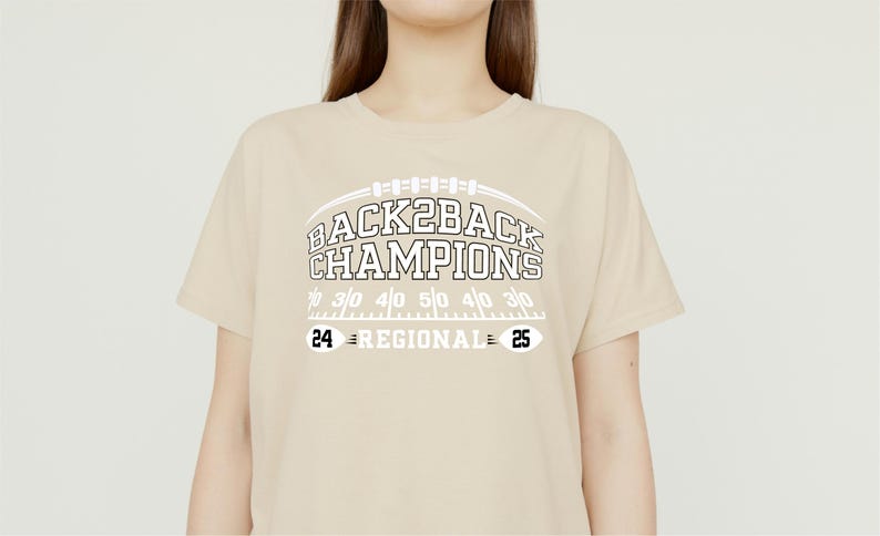 Pu&ograve; includere: T-shirt beige con la scritta bianca "BACK2BACK CHAMPIONS" sopra una grafica di campo da football. Sotto, i numeri "24" e "25" con "REGIONAL" in mezzo. La maglietta &egrave; in stile casual.