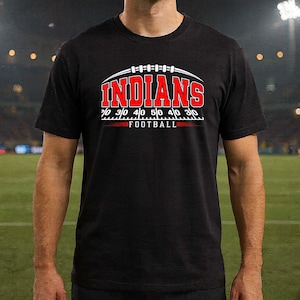 Könnte beinhalten: Ein schwarzes Kurzarm-T-Shirt mit einem Grafikdesign, das das Wort INDIANS in roten Großbuchstaben über einer weißen Grafik einer Football-Spielfeldmarkierung und dem Wort FOOTBALL in weißem Text mit roten horizontalen Linien zeigt.