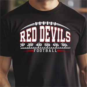 May include: Black t-shirt with the words "RED DEVILS" in large white letters with red accents. Below the text is a football field design with yard markers. The word "FOOTBALL" is written in white.