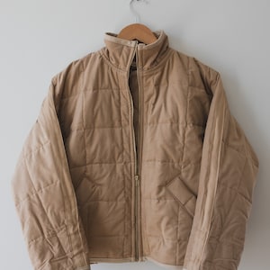 May include: A brown quilted jacket with a zipper closure and a high collar. The jacket has a diamond-shaped quilted pattern and a slightly cropped length.