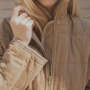 May include: A brown quilted jacket with a zipper closure. The jacket has a high collar and a relaxed fit.