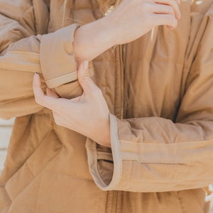 May include: A brown quilted jacket with a zipper closure and a light brown trim around the edges. The jacket is made of a soft, comfortable material.