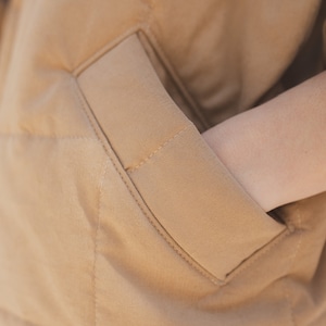 May include: A close-up of a brown quilted jacket with a large pocket on the front. The pocket is angled and has a stitched seam.