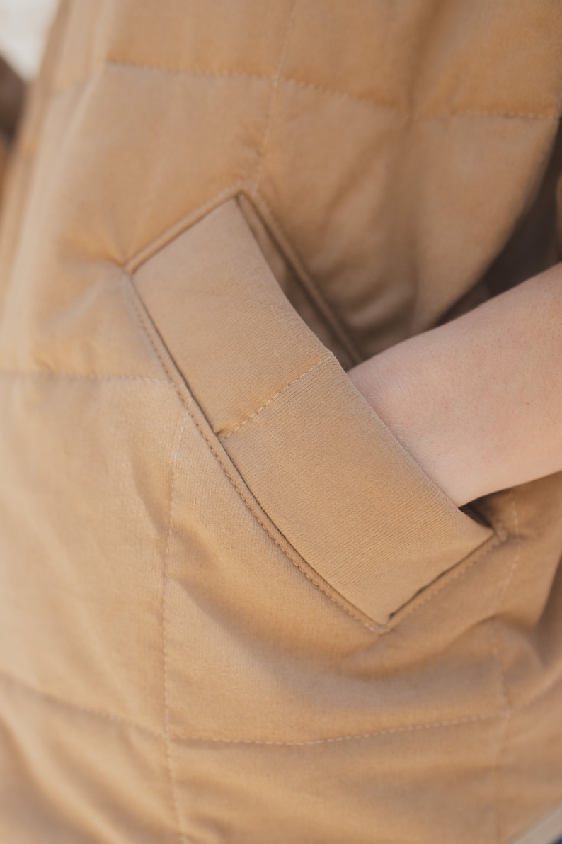 May include: A close-up of a brown quilted jacket with a large pocket on the front. The pocket is angled and has a stitched seam.