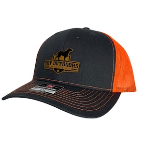 May include: A black and orange trucker hat with a gold logo that says "GET OUTDOORS" with a silhouette of a dog inside a shield. The logo also says "2 Seasons Design".