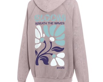 May include: A mauve hooded sweatshirt featuring a back graphic with the text BLOOM BENEATH THE WAVES and JENVAE. The design includes stylized white and light blue flowers with dark purple stems and leaves on a washed-out fabric background.
