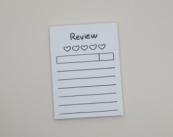 May include: A white notecard with black ink. The notecard has the word "Review" written at the top. Below the word "Review" are five empty heart shapes. Below the hearts is a blank line with a box at the end. The notecard has 10 lines for writing.