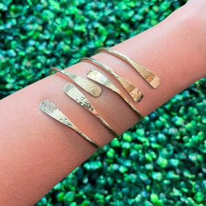 May include: Four gold hammered metal bracelets with a pointed end. The bracelets are stacked on a person's arm.