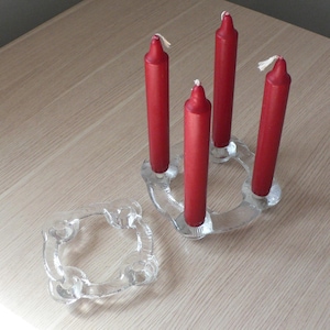 Puede incluir: Un portavelas de vidrio transparente con cuatro velas rojas. El portavelas tiene forma de anillo con cuatro brazos.