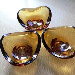 Puede incluir: Tres candelabros de vidrio ámbar en forma de corazón. Los candelabros están sobre una superficie de madera.