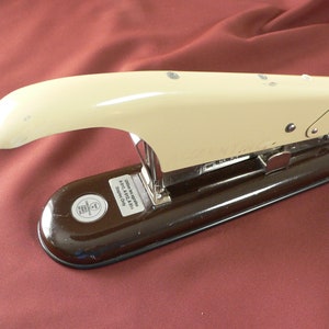 May include: A vintage stapler with a cream-colored top and a dark brown base. The stapler has a curved handle and a metal mechanism. The text on the base reads "A.010, A.012, A.014 Staples Only".