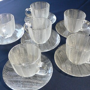 Puede incluir: Juego de seis tazas de té y platillos de vidrio transparente con un patrón de espiga. Las tazas y los platillos son todos del mismo tamaño y forma.