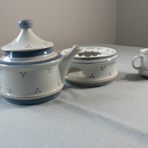 Peut inclure: Service à thé en céramique blanche avec des accents bleus et rouges. L'ensemble comprend une théière avec couvercle, un chauffe-plat et un petit pot à crème. Chaque pièce est ornée de petits points gris.