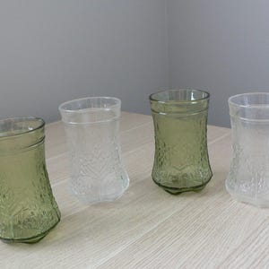 May include: Four clear glass drinking glasses with a textured design. Two glasses are green and two are clear.