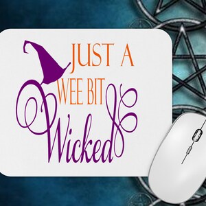 May include: A white mouse mat with the text "Just a wee bit wicked" in orange and purple lettering. A purple witch's hat is above the text.