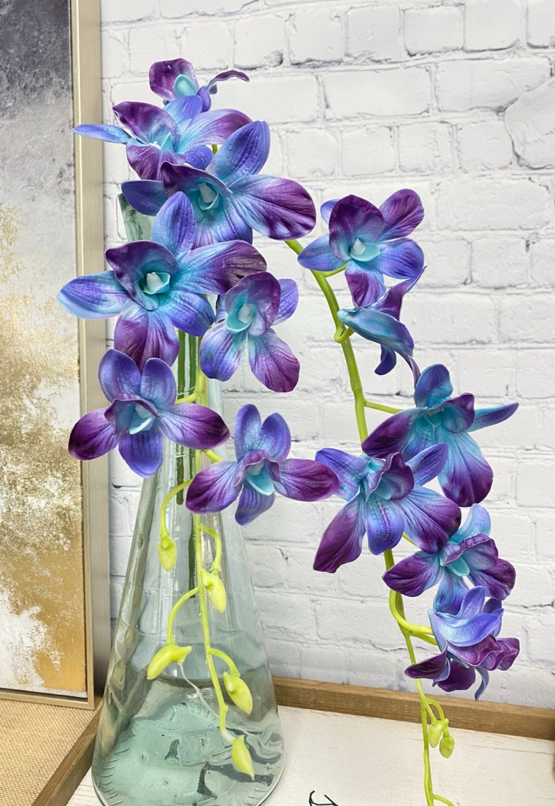 May include: A bouquet of blue and purple orchids in a clear glass vase. The orchids have a gradient of color from blue to purple.