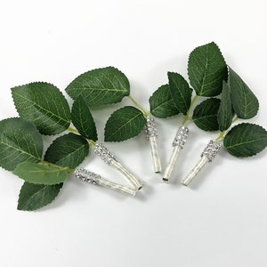 May include: Five artificial rose stems with green leaves and white stems with silver rhinestone accents.