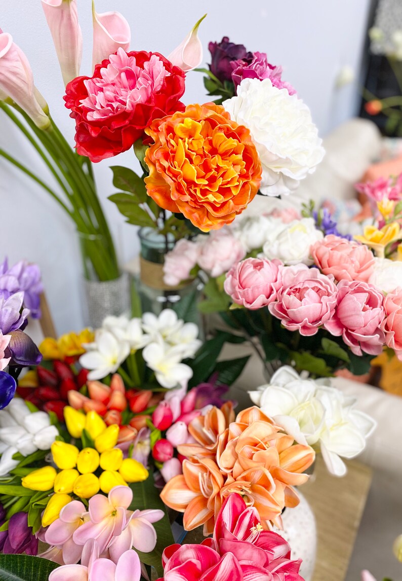 May include: A bouquet of artificial flowers in various colors, including pink, orange, yellow, and white. The flowers are arranged in a vase and include peonies, lilies, and tulips.