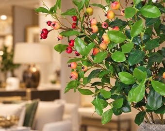 Puede incluir: Una planta artificial decorativa con hojas verdes vibrantes y una mezcla de pequeñas bayas rojas, naranjas y blancas. La planta se presenta en una maceta texturizada de color gris con aspecto de piedra, mostrando detalles botánicos realistas.