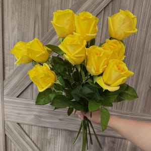 May include: A bouquet of vibrant yellow roses with green foliage. The roses are fully open, and the stems are bound together. The backdrop is a wooden door.
