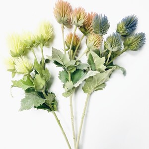 Puede incluir: Un ramo de flores artificiales con hojas verdes. Las flores son en tonos de azul, rosa y amarillo.