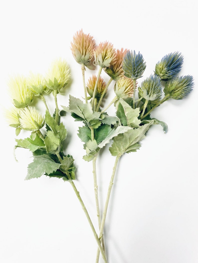 Puede incluir: Un ramo de flores artificiales con hojas verdes. Las flores son en tonos de azul, rosa y amarillo.