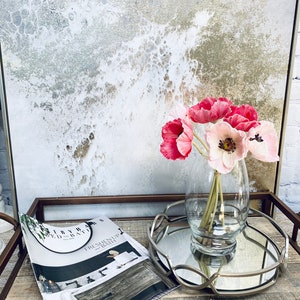 May include: A glass vase filled with pink and white silk flowers sits on a silver tray with a magazine on a wooden surface.