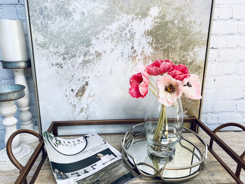 May include: A glass vase filled with pink and white silk flowers sits on a silver tray with a magazine on a wooden surface.
