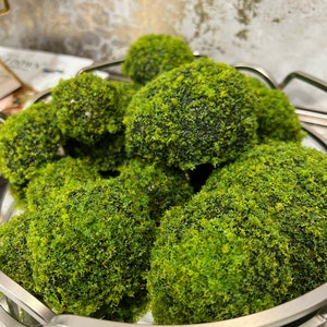 May include: A silver bowl filled with round, green moss balls. The moss balls are arranged in a decorative pattern.
