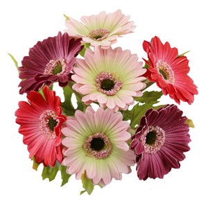 May include: A bouquet of seven artificial gerbera daisies in various shades of pink, red, and purple. The flowers have a realistic appearance and are arranged in a cluster.