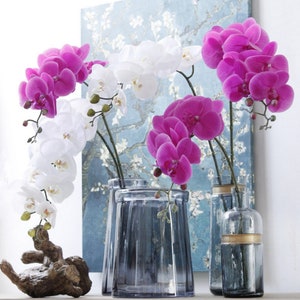 May include: Three glass vases with artificial orchid flowers. The vases are clear glass with a textured surface. The flowers are white and pink.