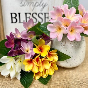 May include: A bouquet of artificial flowers in a white ceramic vase. The flowers are pink, purple, white, and yellow. The vase has a speckled pattern. The flowers are arranged in a vase with a sign that says "Simply Blessed" in the background.