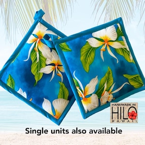May include: A pair of blue pot holders with a white floral pattern. The pot holders have a turquoise border and are handmade in Hilo, Hawaii.