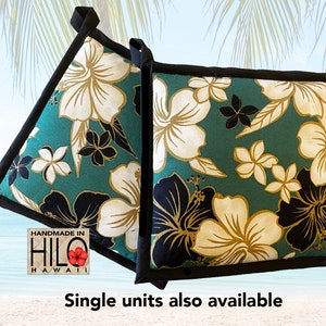 May include: Two teal blue pot holders with a black border and a white and gold hibiscus floral print. The pot holders are handmade in Hilo, Hawaii.