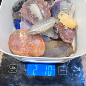 Pu&ograve; includere: Una bilancia digitale che mostra 2,10 oz con una ciotola bianca piena di varie pietre di agata e diaspro colorate.