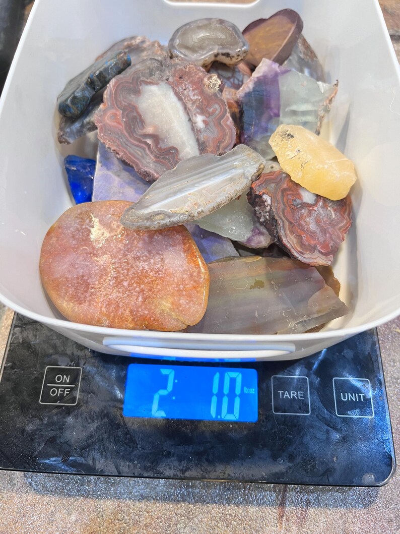 Pu&ograve; includere: Una bilancia digitale che mostra 2,10 oz con una ciotola bianca piena di varie pietre di agata e diaspro colorate.