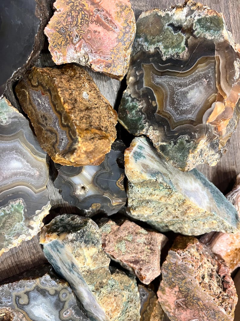 Pu&ograve; includere: Una collezione di fette di agata in varie tonalit&agrave; di verde, marrone e rosa. Le fette di agata presentano motivi e trame intricate.