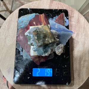 Pu&ograve; includere: Una bilancia da cucina digitale con un display blu che mostra 2,19. Un mucchio di piastrelle di ceramica colorate e rotte si trova sulla bilancia.