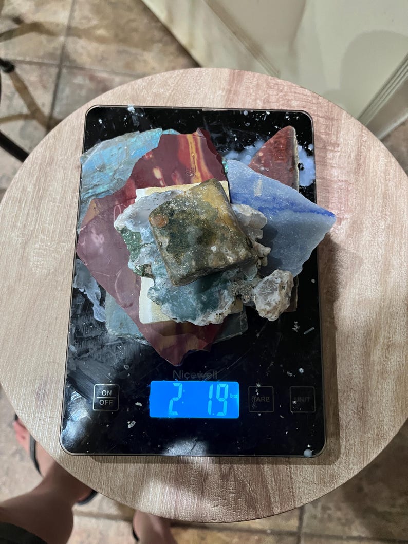 Pu&ograve; includere: Una bilancia da cucina digitale con un display blu che mostra 2,19. Un mucchio di piastrelle di ceramica colorate e rotte si trova sulla bilancia.
