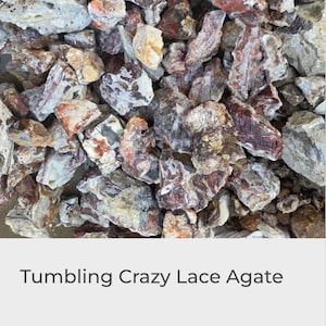 Puede incluir: Un montón de piedras de ágata Crazy Lace pulidas. Las piedras muestran una variedad de colores, incluyendo blanco, beige, marrón y marrón rojizo. Las piedras tienen una textura rugosa y natural y formas irregulares. El texto "Tumbling Crazy Lace Agate" está en la parte inferior.