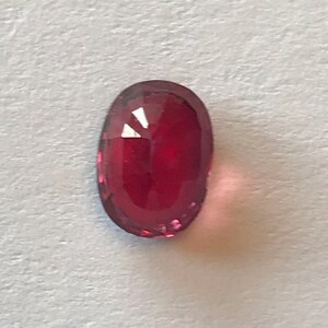 May include: A deep red oval-shaped gemstone with a faceted cut.