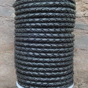 Puede incluir: Primer plano de un carrete de cordón de cuero trenzado negro. El cordón está enrollado apretado y tiene un acabado liso y pulido.