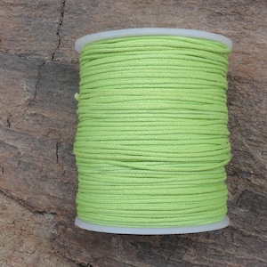 Può includere: Un rocchetto di cordoncino di cotone cerato verde brillante. Il cordoncino è avvolto strettamente attorno a un rocchetto di plastica bianca.