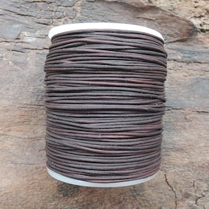 Puede incluir: Un carrete de cordón de cuero marrón, enrollado apretado y listo para proyectos de artesanía.